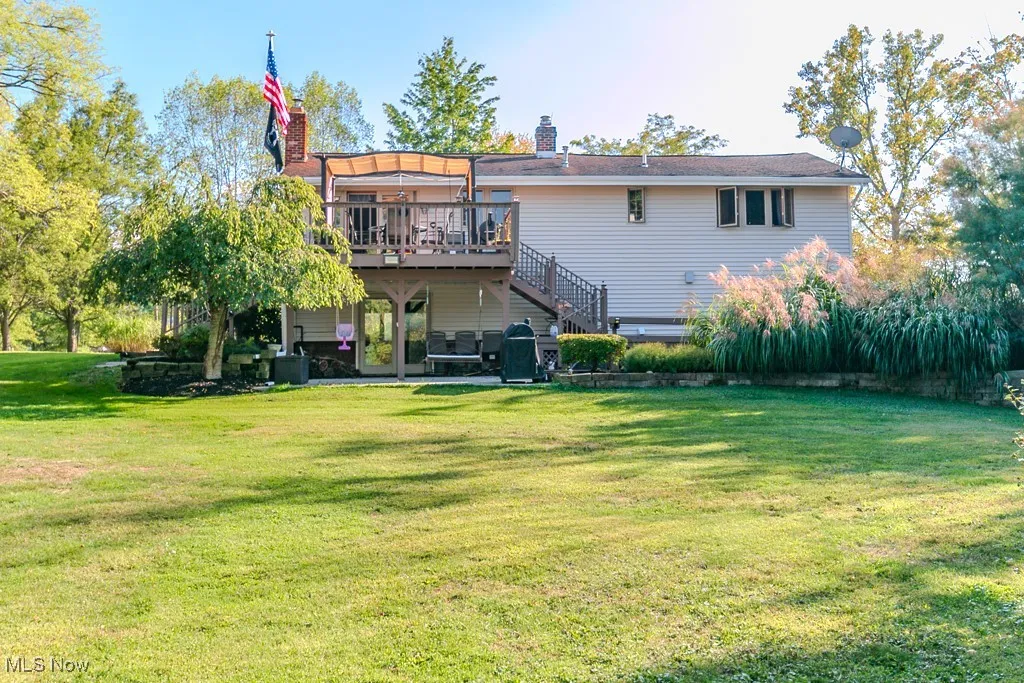 Back of house featuring a patio area, a deck, a yard, stairs, and a chimney