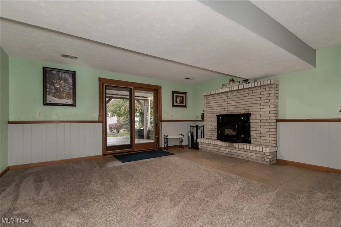 Unfurnished living room with a textured ceiling, tile patterned floors, carpet, a wainscoted wall, and a brick fireplace