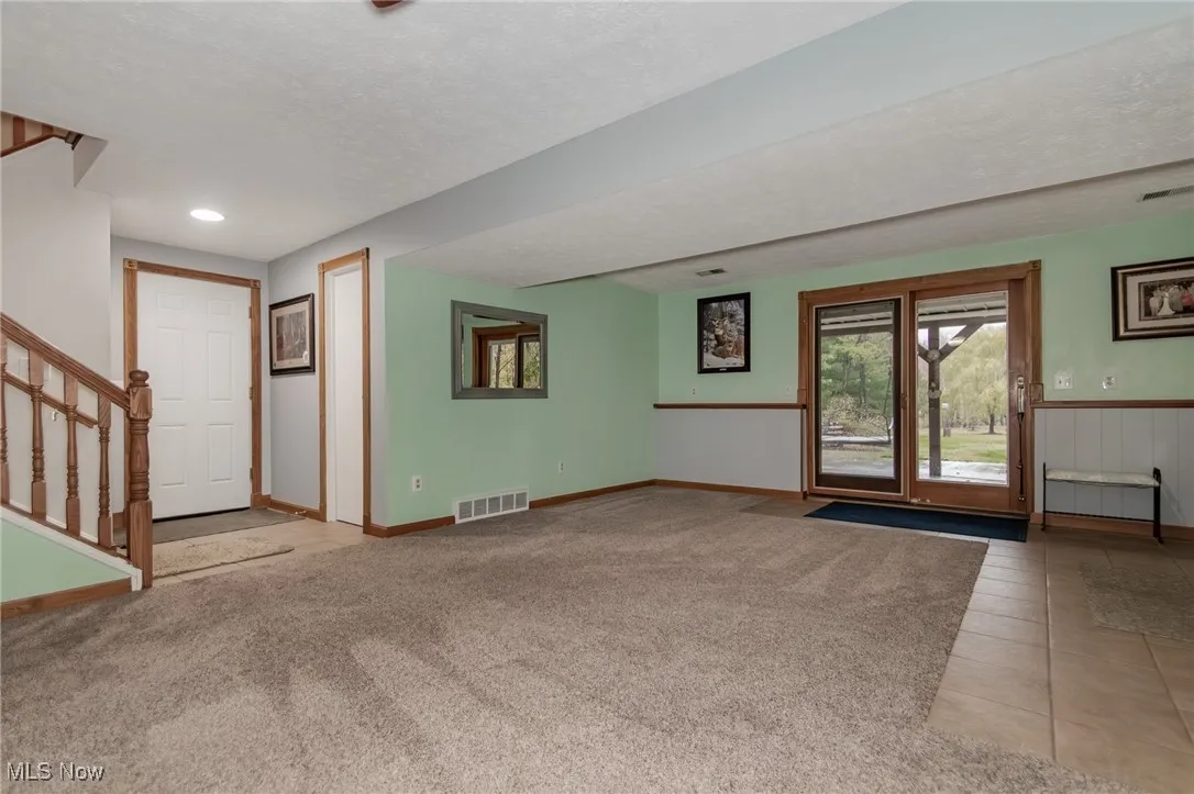 Unfurnished living room featuring stairway, a textured ceiling, light carpet, and light tile patterned floors
