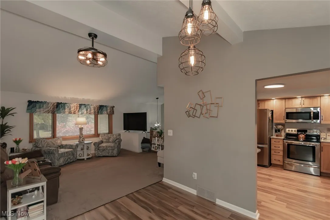 Living room featuring light wood-style flooring, a chandelier, beam ceiling, and high vaulted ceiling