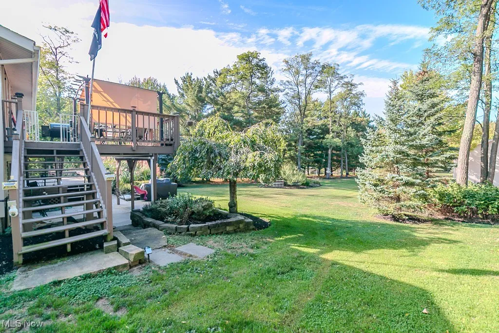 View of green lawn with a patio area, a deck, and stairway