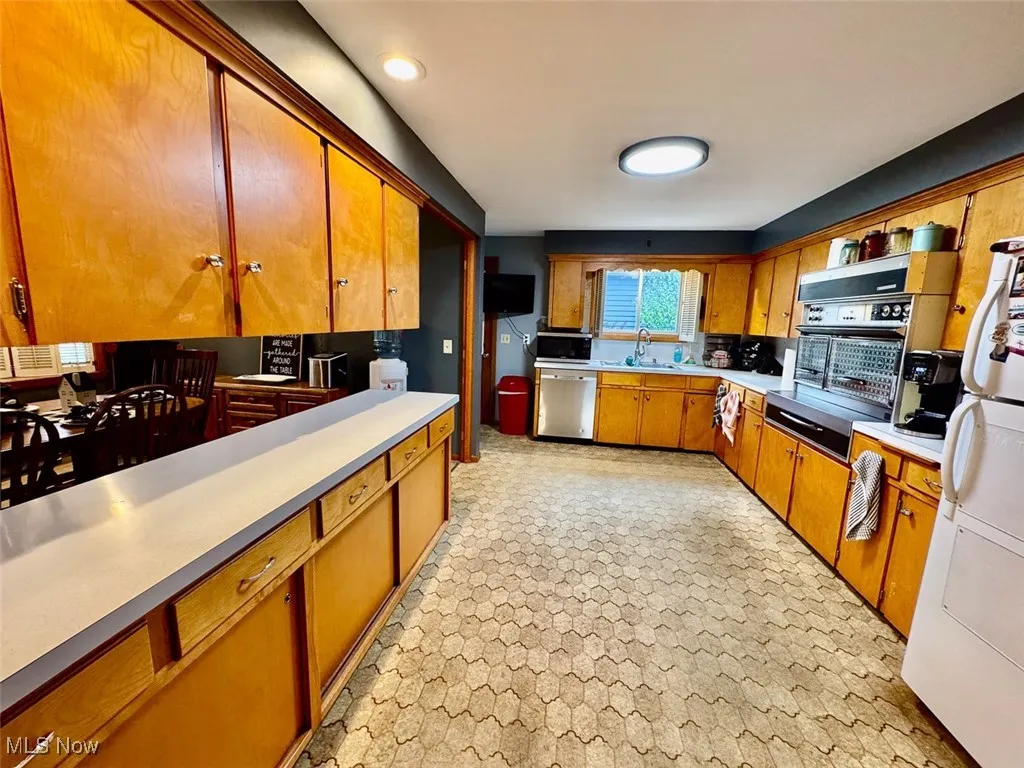 Kitchen with brown cabinetry, light countertops, stainless steel appliances, recessed lighting, and a warming drawer