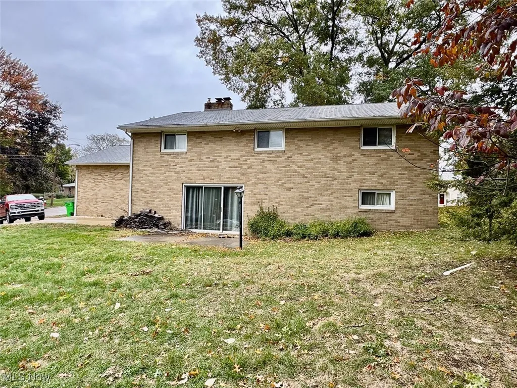 Back of property with brick siding, a lawn, and a chimney