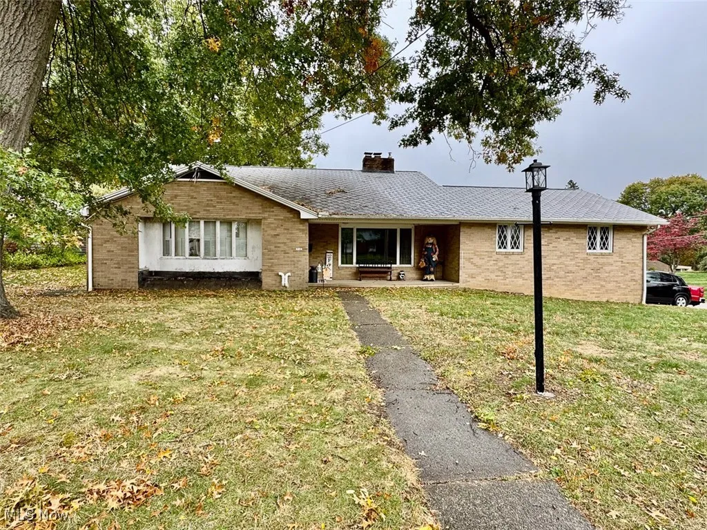 Ranch-style home featuring a front yard, a chimney, covered porch, and brick siding