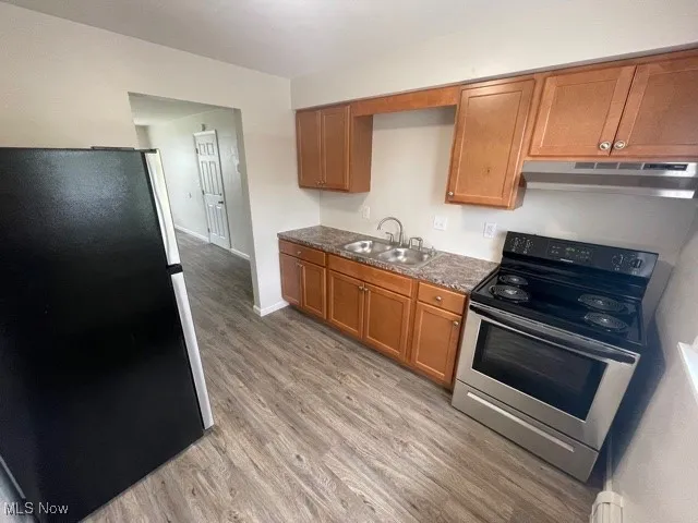 Kitchen with stainless steel appliances, dark countertops, brown cabinets, light wood-style floors, and under cabinet range hood
