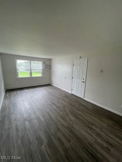 Empty room with dark wood-style floors, baseboard heating, and a wall mounted AC
