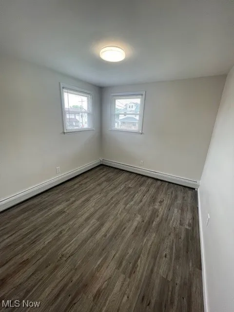 Spare room featuring dark wood-style floors, baseboard heating, and a baseboard radiator