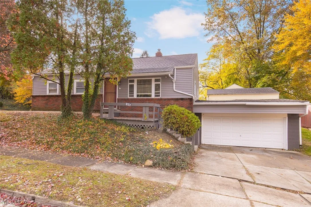 View of front facade with a chimney, driveway, brick siding, an attached garage, and roof with shingles