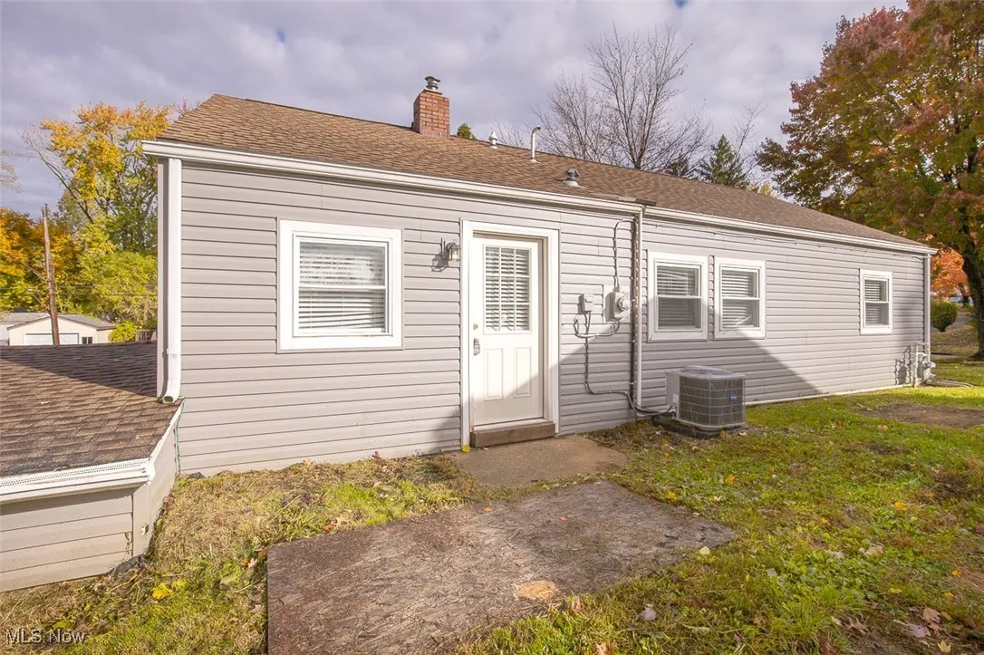 Back of property with roof with shingles, a chimney, and a lawn