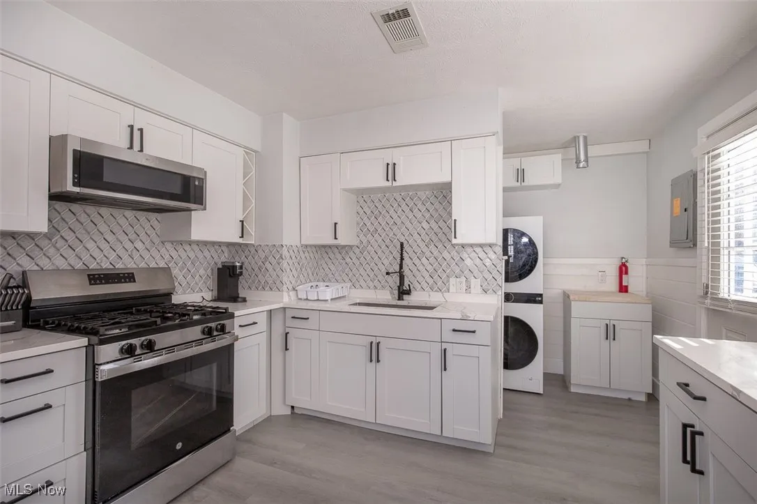 Kitchen featuring appliances with stainless steel finishes, light wood-style floors, white cabinets, and stacked washing machine and dryer