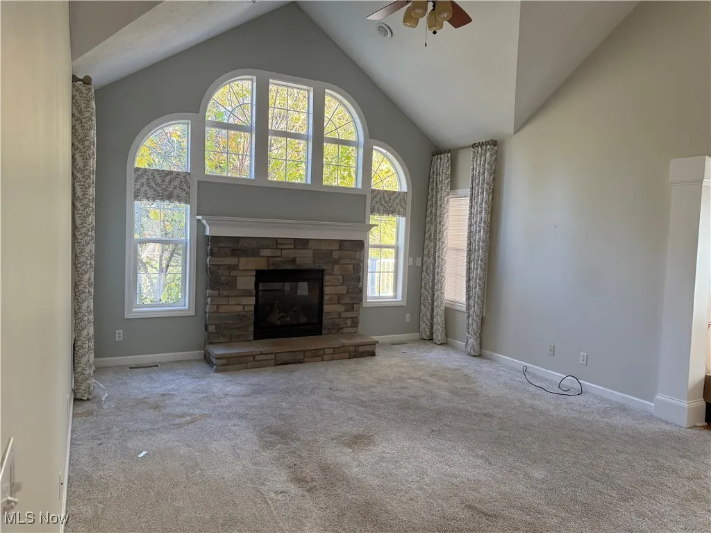 Unfurnished living room featuring high vaulted ceiling, carpet flooring, ceiling fan, and a stone fireplace