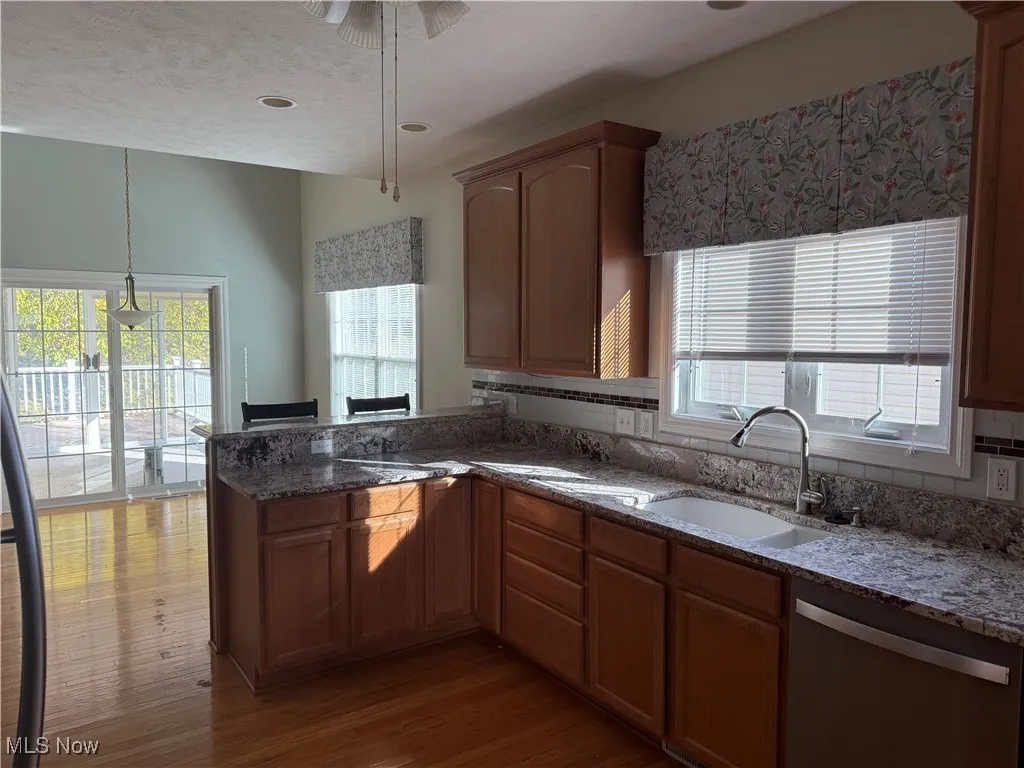 Kitchen with healthy amount of natural light, dark stone countertops, dishwasher, dark wood finished floors, and a textured ceiling