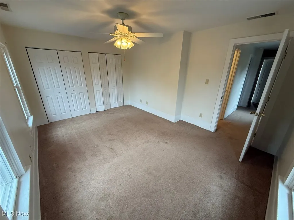 Unfurnished bedroom with carpet flooring, multiple closets, and ceiling fan