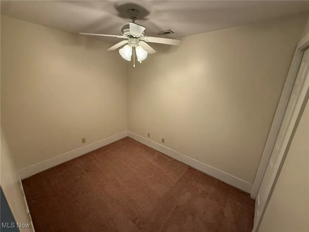 Unfurnished room with dark colored carpet and ceiling fan