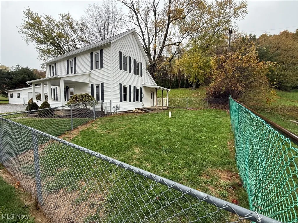 View of side of property with a fenced backyard, a porch, and view of wooded area