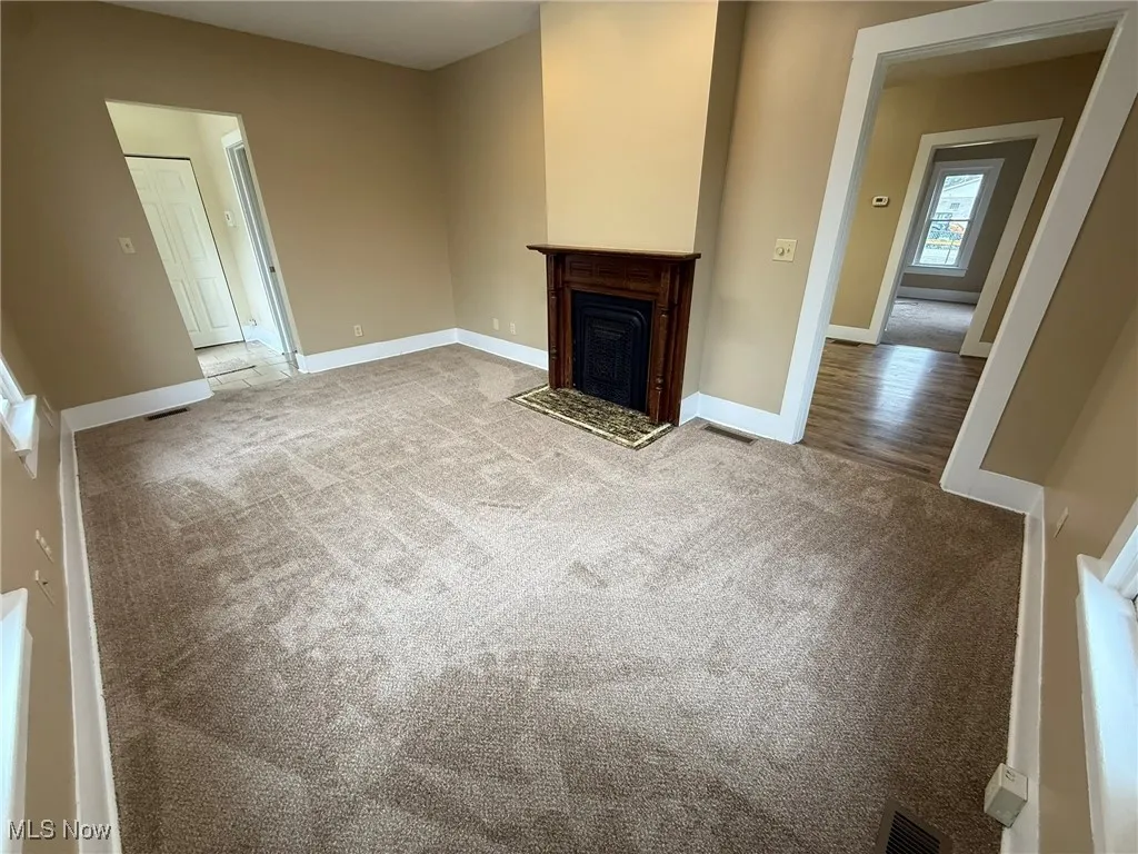 Unfurnished living room with carpet and a fireplace with flush hearth