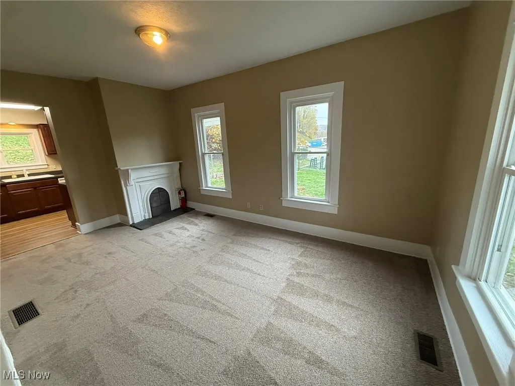 Unfurnished living room featuring plenty of natural light, a fireplace, and light colored carpet