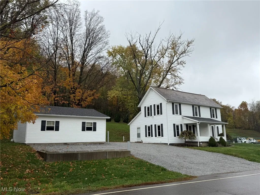 View of side of property featuring a yard, a porch, and gravel driveway