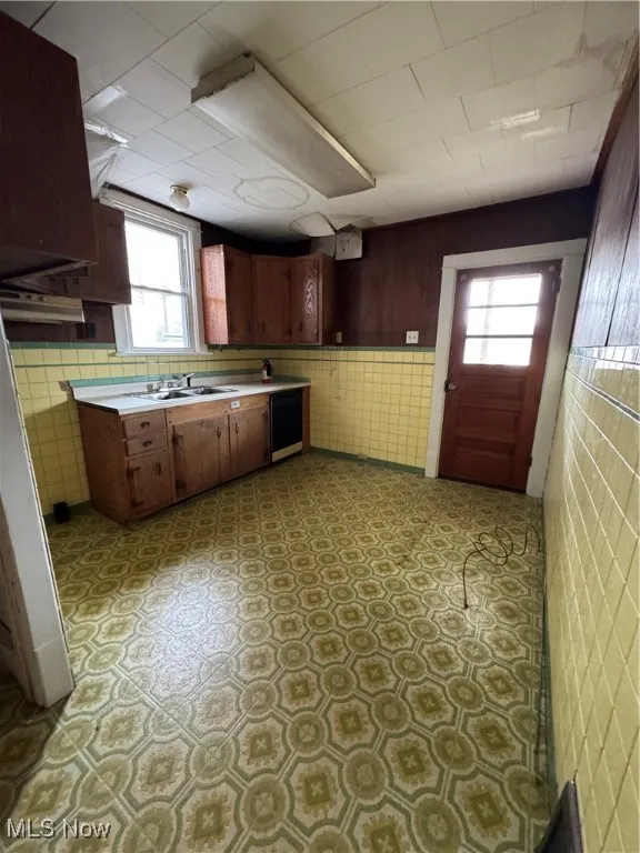 Kitchen featuring light countertops, healthy amount of natural light, dishwasher, light floors, and tile walls