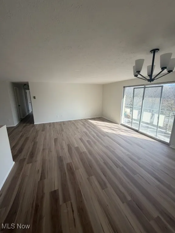 Unfurnished living room with dark wood-style flooring, a chandelier, and a textured ceiling