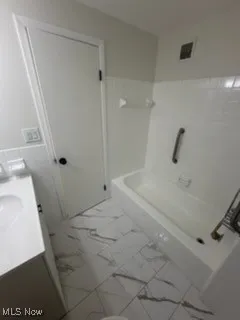 Full bathroom featuring vanity, light marble finish floors, tile walls, and shower / bathtub combination