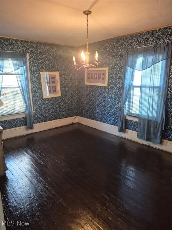 Unfurnished dining area featuring dark wood-style flooring, a chandelier, and wallpapered walls