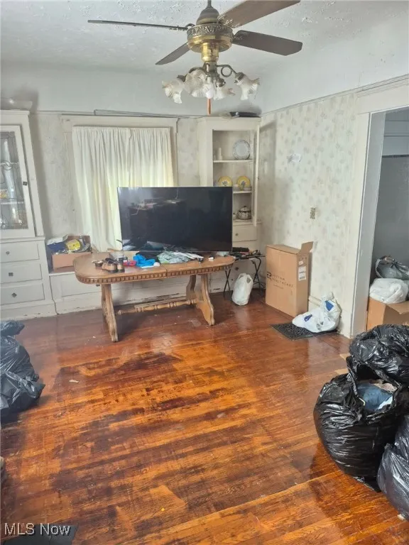 Living area with dark wood-type flooring, a textured ceiling, ceiling fan, and wallpapered walls