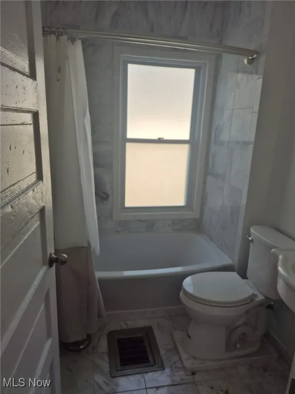 Bathroom with shower / bath combo with shower curtain and marble look tiles