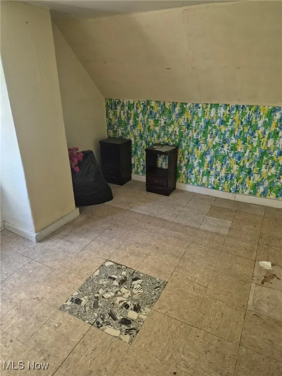 Additional living space with wallpapered walls and vaulted ceiling