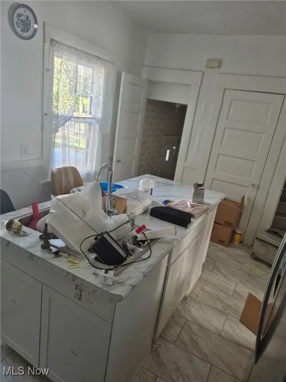 Kitchen featuring white cabinetry, an island with sink, and freestanding refrigerator