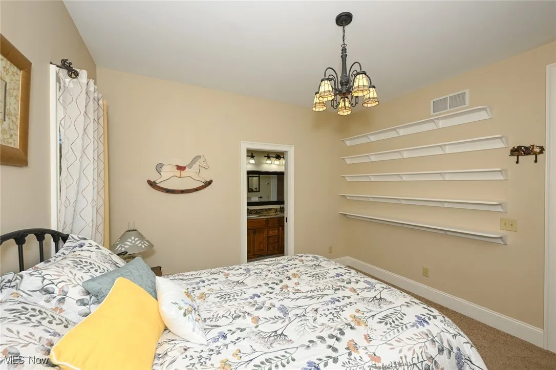 Bedroom featuring a chandelier, light carpet, and ensuite bathroom