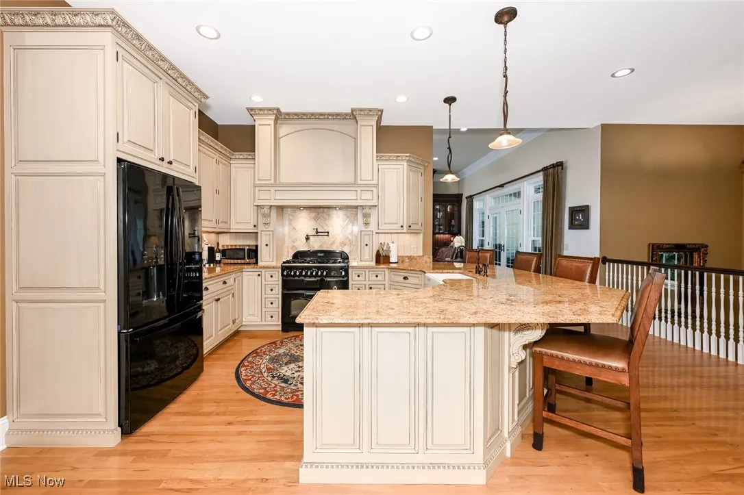Kitchen with cream cabinets, black appliances, decorative light fixtures, a breakfast bar area, and backsplash