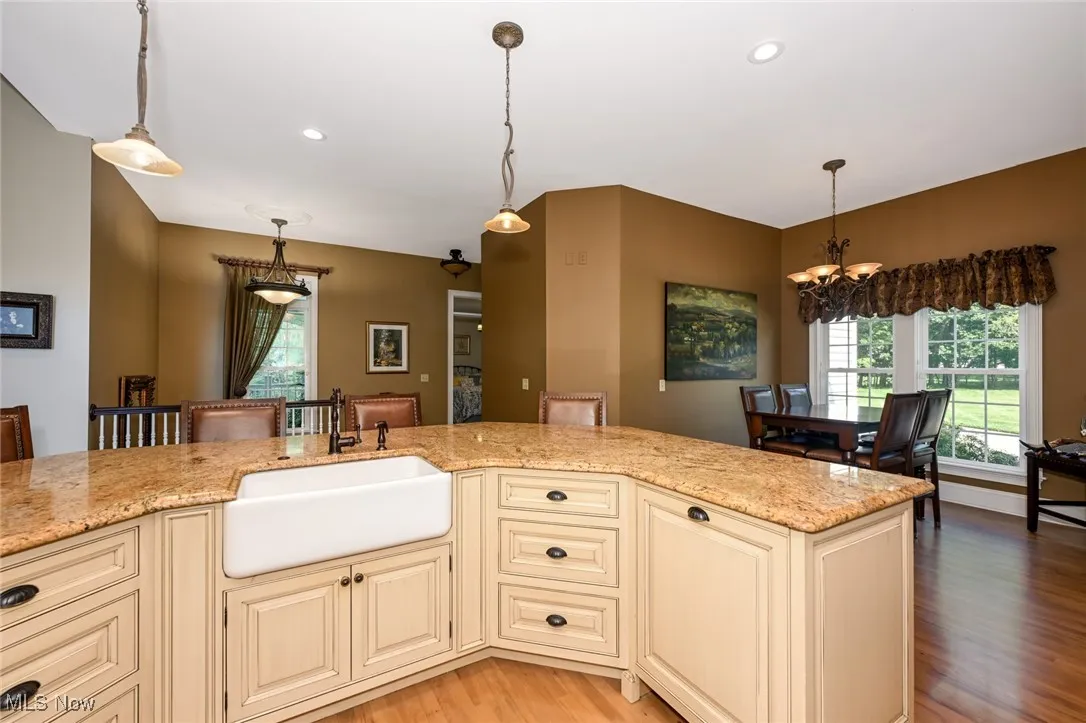 Kitchen with cream cabinetry, pendant lighting, light stone countertops, light wood-style flooring, and a chandelier