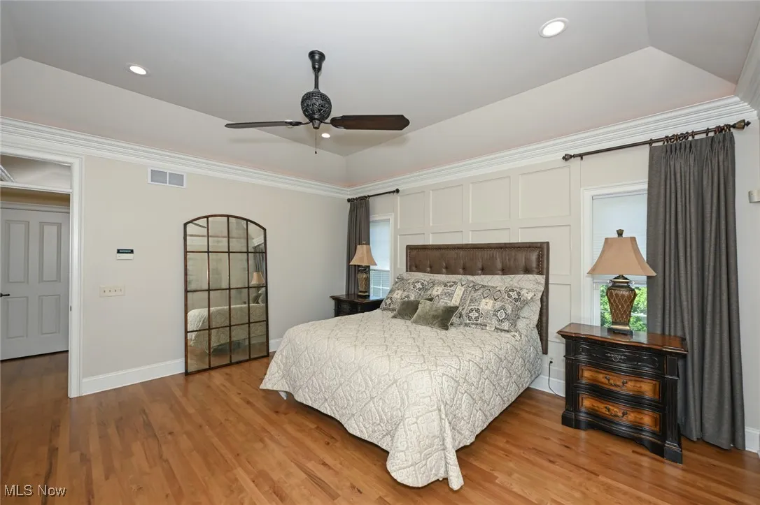 Bedroom with a raised ceiling, wood finished floors, ceiling fan, recessed lighting, and ornamental molding