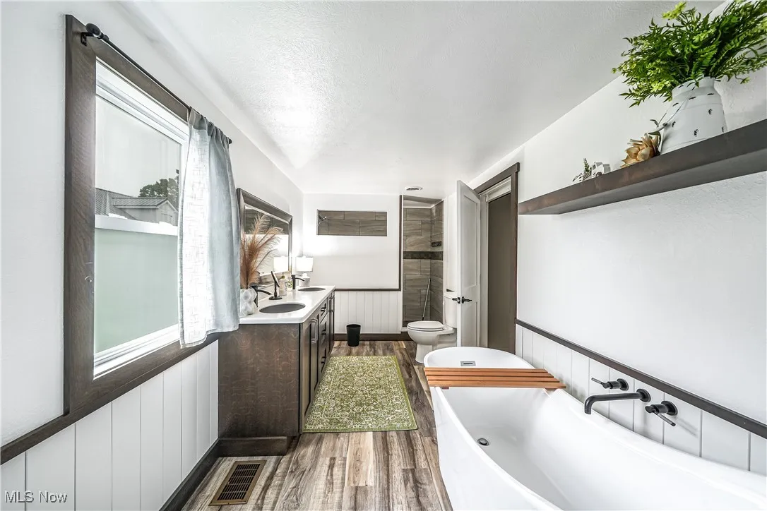 Full bathroom with wainscoting, dark wood-type flooring, double vanity, a freestanding bath, and a tile shower