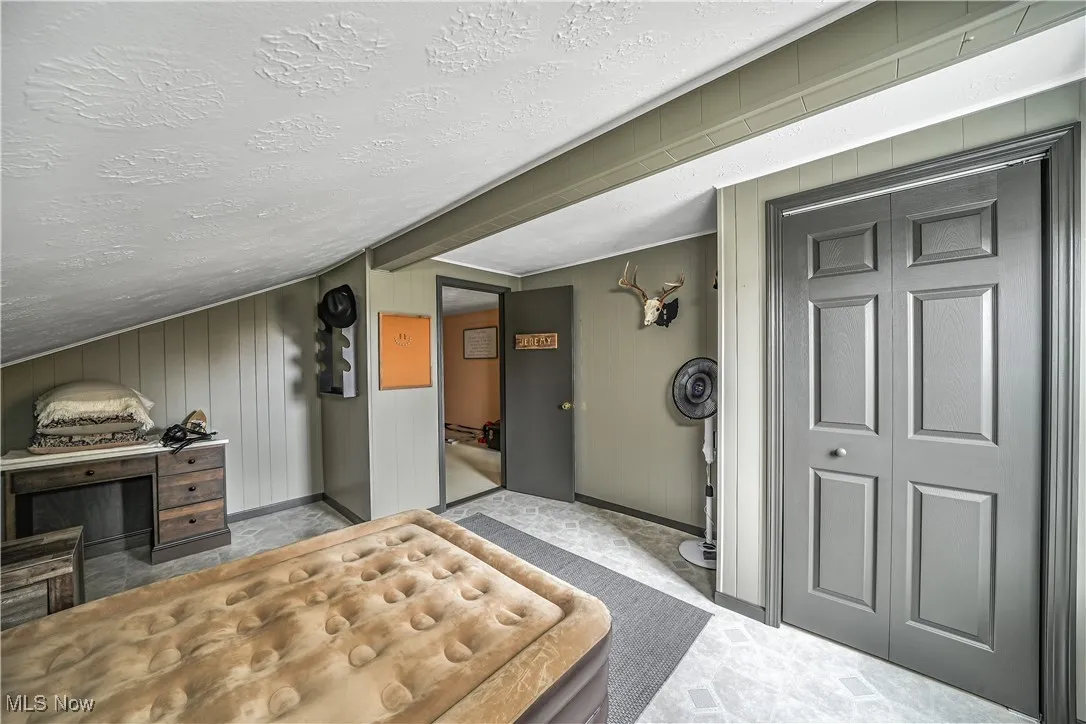 Bedroom featuring a closet, a textured ceiling, vaulted ceiling, and wood walls