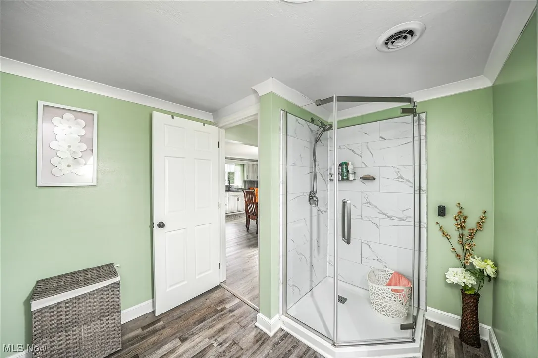Bathroom with dark wood-style flooring, a marble finish shower, and crown molding