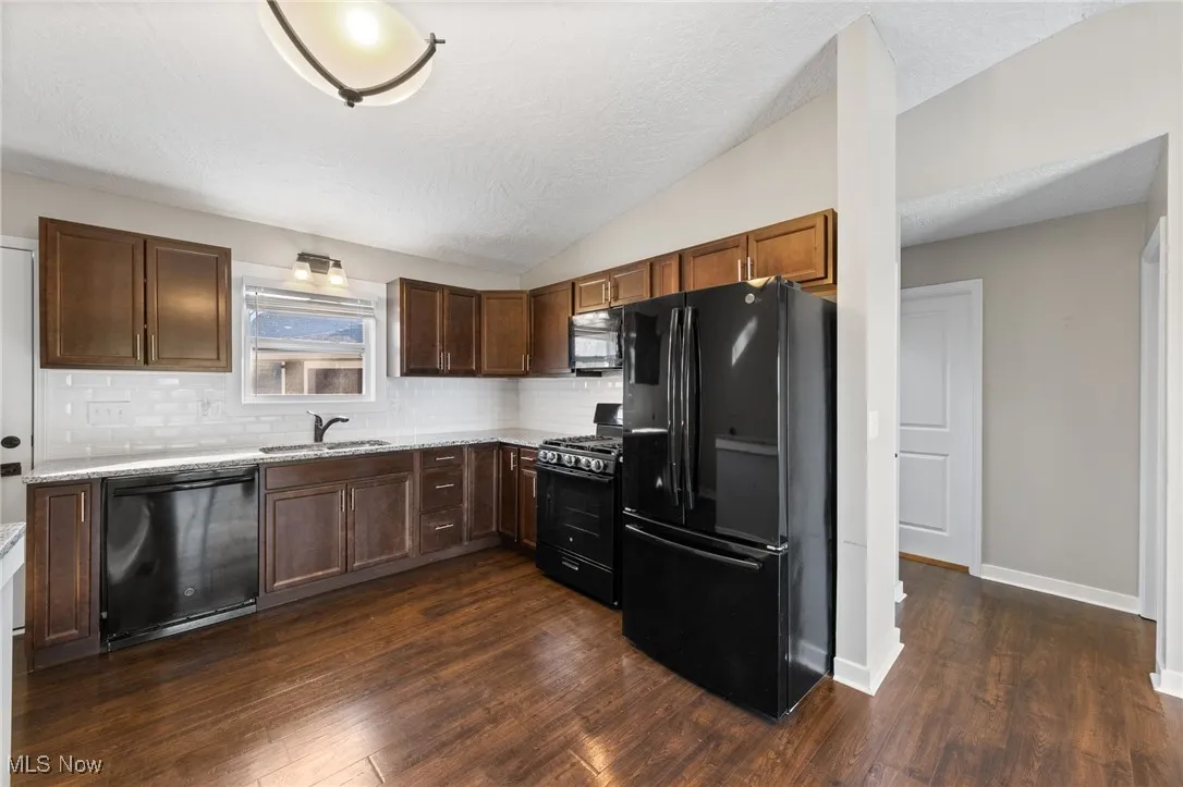 Kitchen featuring black appliances, vaulted ceiling, tasteful backsplash, dark wood-style floors, and a textured ceiling