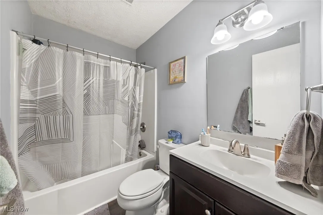 Full bathroom featuring a textured ceiling, shower / bath combination with curtain, and vanity