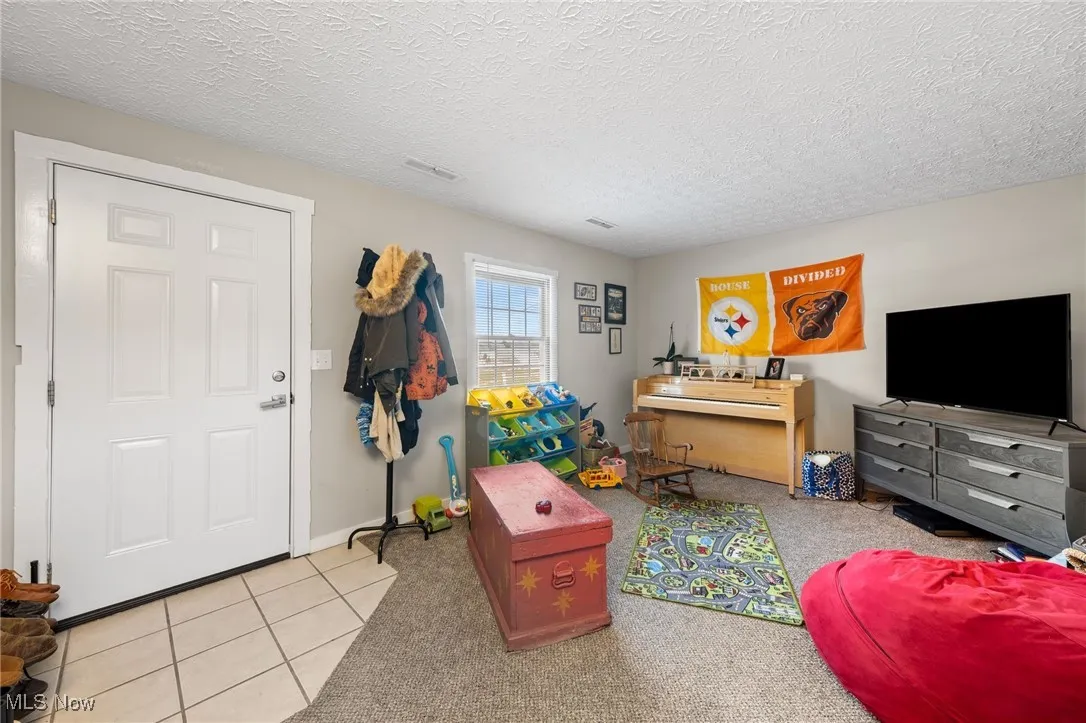 Recreation room with a textured ceiling, light colored carpet, and light tile patterned floors