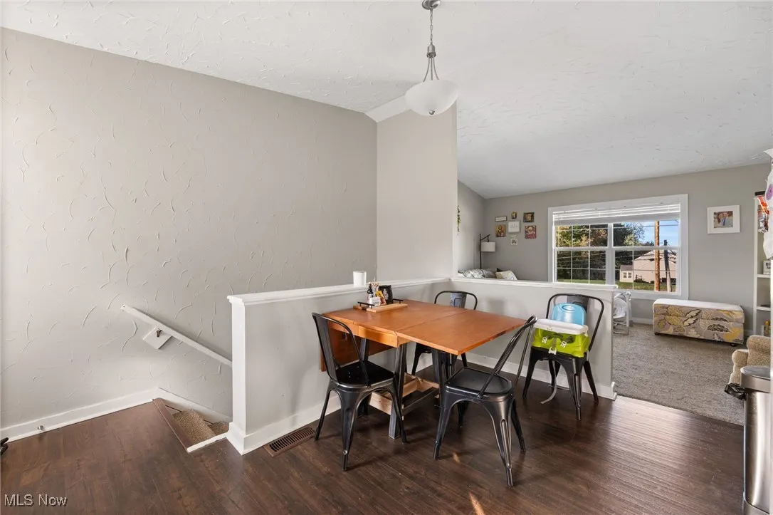 Dining room with a textured wall, dark wood finished floors, a textured ceiling, and vaulted ceiling