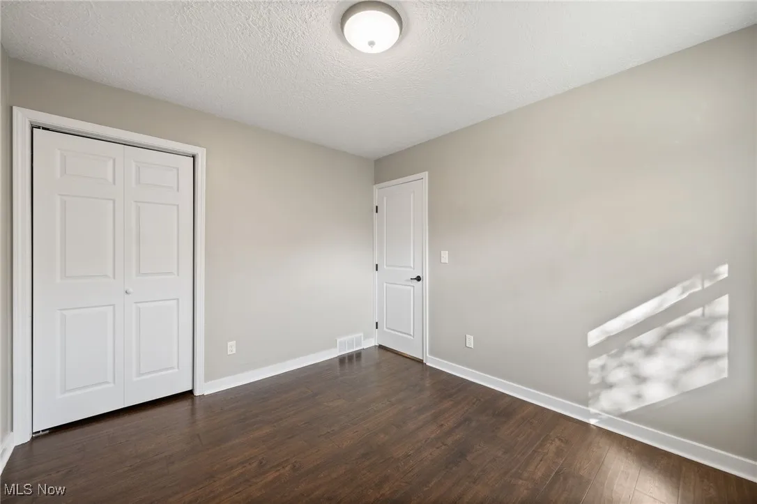 Unfurnished bedroom featuring a textured ceiling, dark wood-type flooring, and a closet