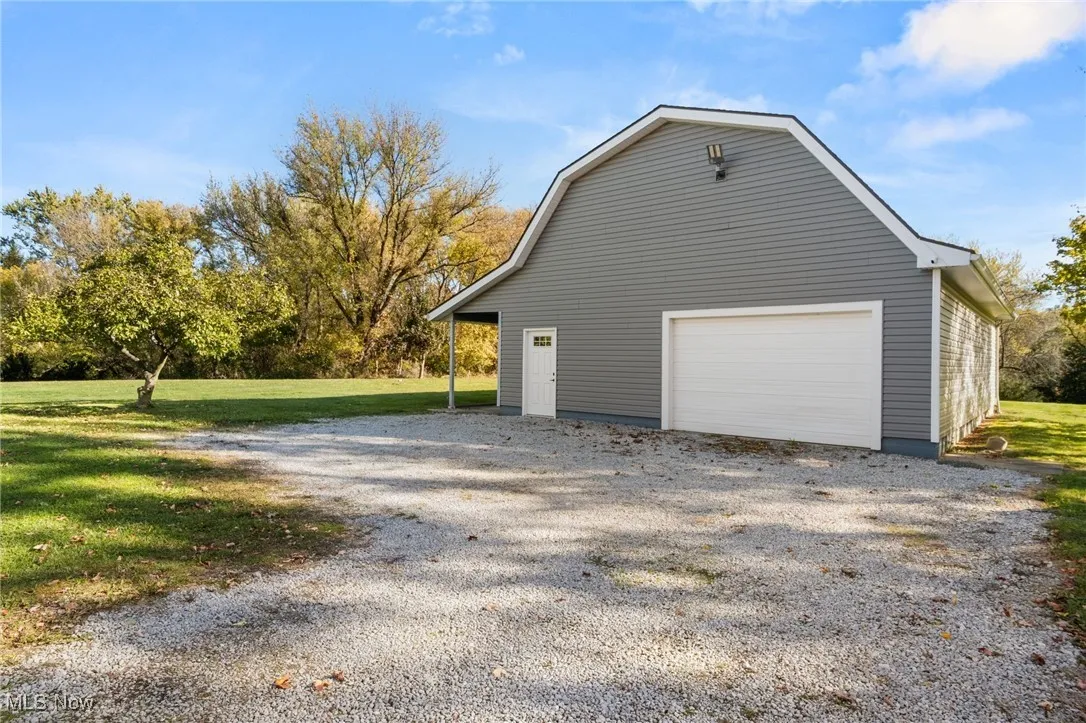 View of side of home featuring a gambrel roof, an outbuilding, a yard, a garage, and gravel driveway