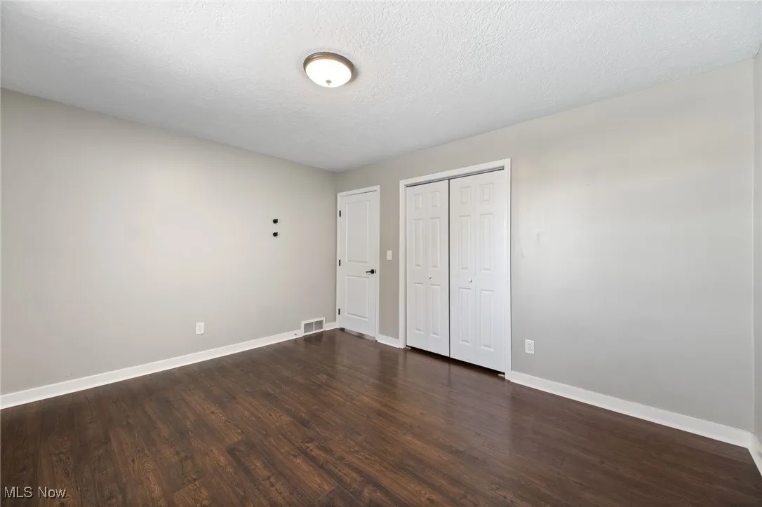 Unfurnished bedroom featuring a textured ceiling, dark wood-style floors, and a closet