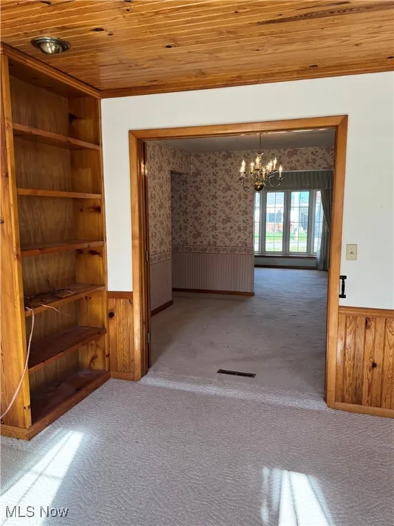 Carpeted spare room with wainscoting, wood walls, a chandelier, and wood ceiling