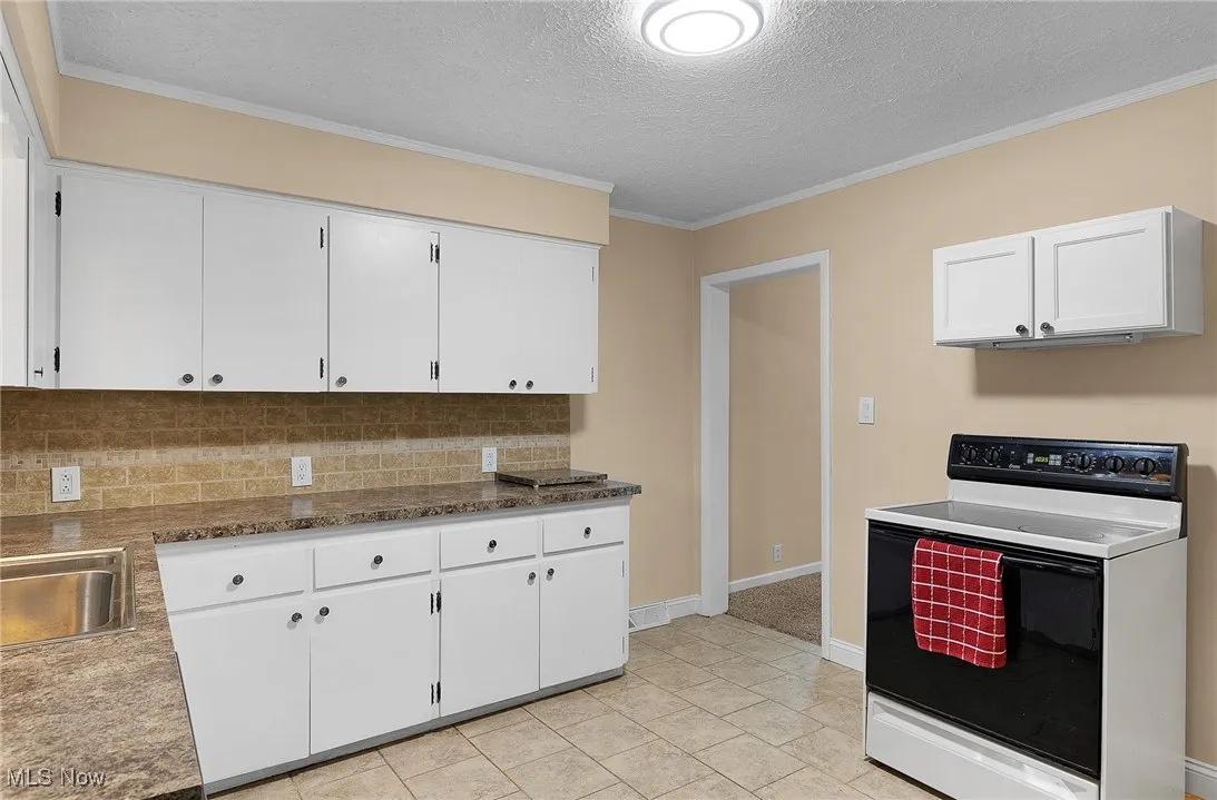 Kitchen featuring range with electric cooktop, ornamental molding, white cabinets, a textured ceiling, and backsplash