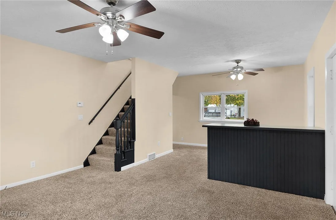 Unfurnished living room featuring carpet, ceiling fan, and stairs