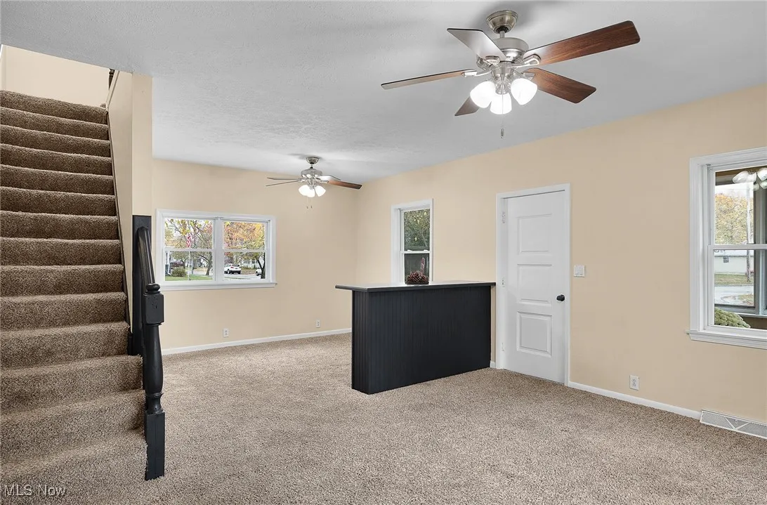 Unfurnished living room featuring stairs, light carpet, ceiling fan, and a textured ceiling