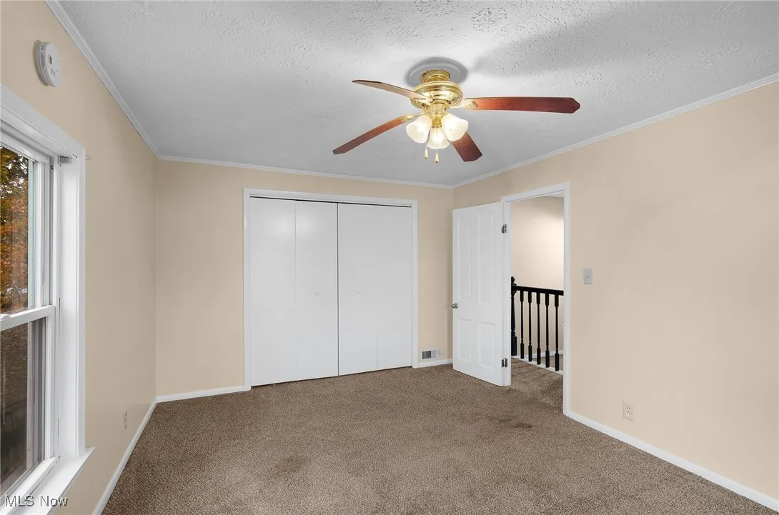 Unfurnished bedroom with ornamental molding, a textured ceiling, carpet, a closet, and a ceiling fan