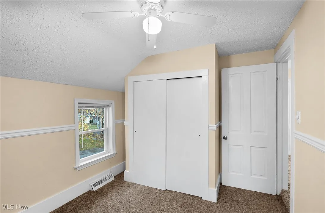 Unfurnished bedroom featuring a textured ceiling, carpet flooring, a closet, lofted ceiling, and ceiling fan